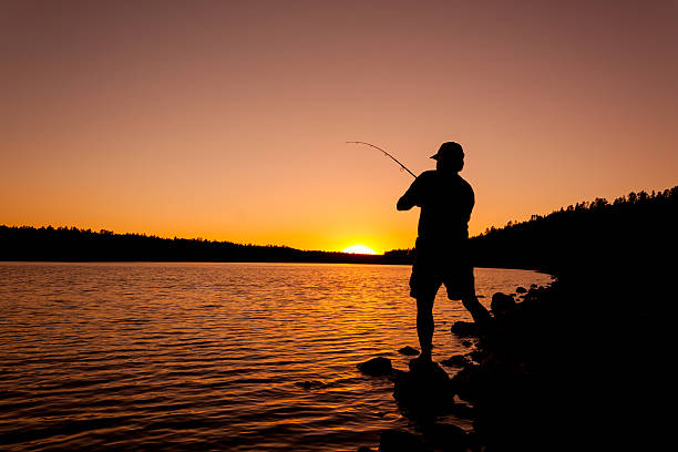 a fisherman fighting a fish at sunset
